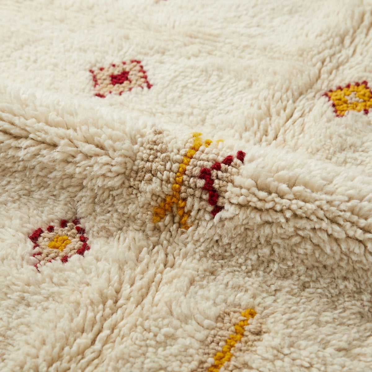 Detail of Moroccan wool rug, small yellow, orange and red motifs on a cream wool ground