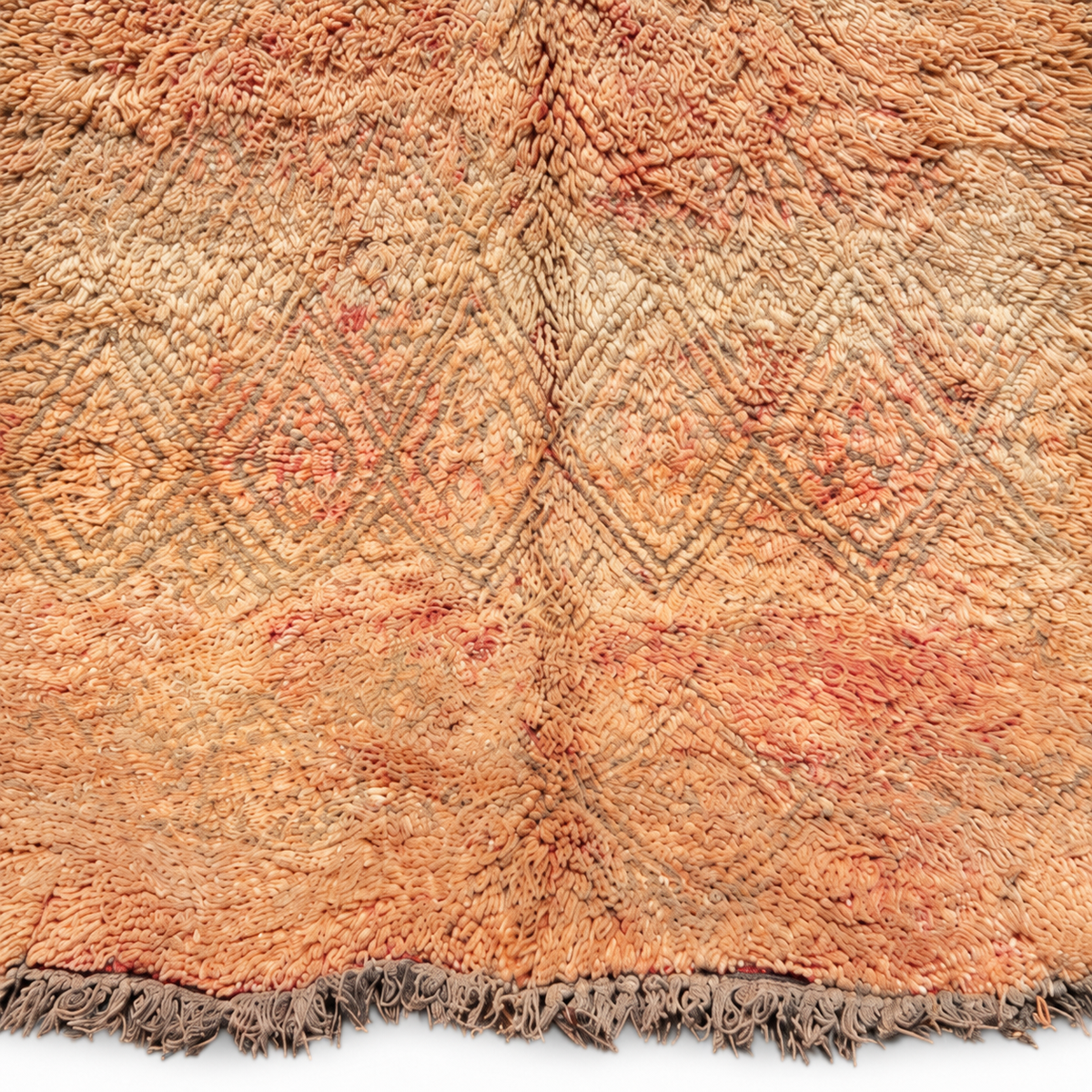 Close-up of the faded diamond pattern and peach accents on the beige vintage Moroccan rug.